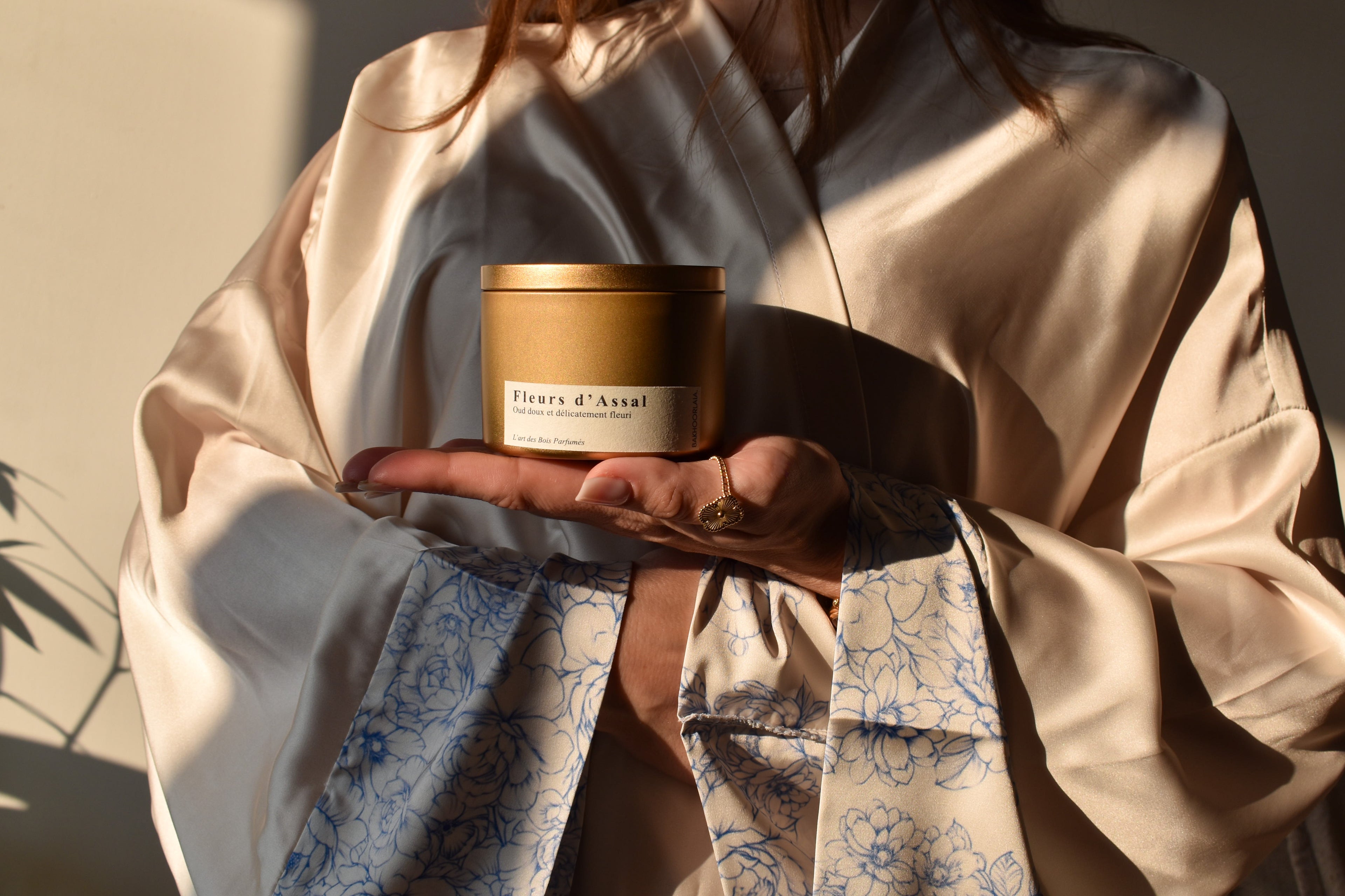 Une femme portant une abaya de luxe en soie avec un pot de bakhoor a base de oud et de fleurs.